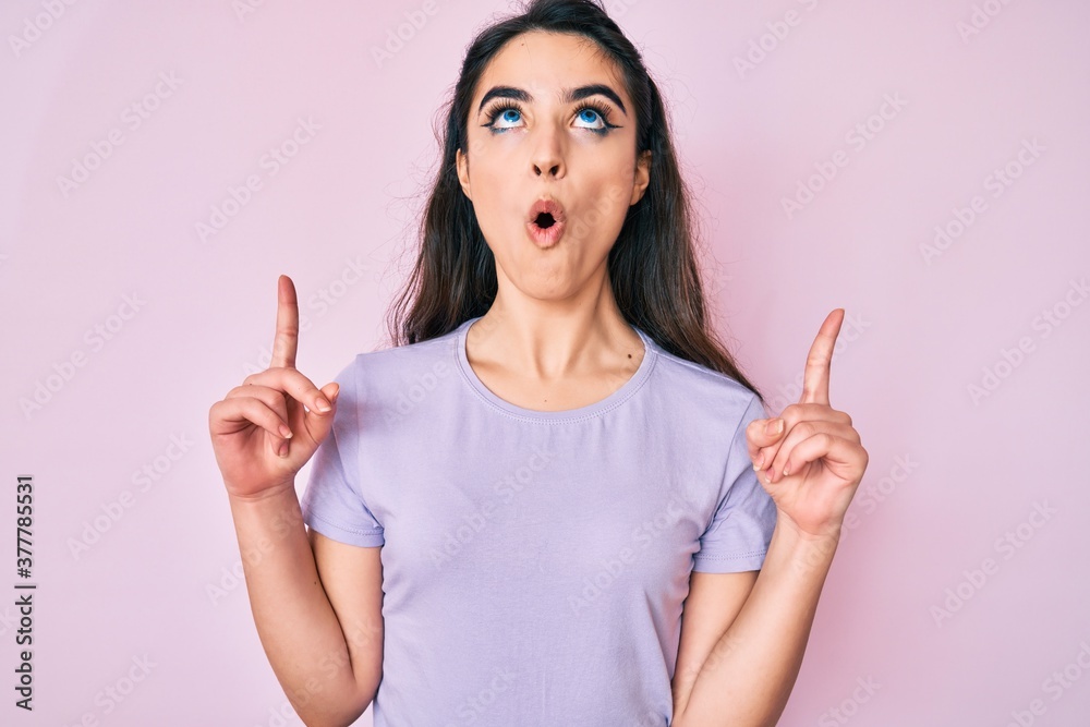 Brunette teenager girl wearing casual clothes amazed and surprised looking up and pointing with fingers and raised arms. Brunette teenager girl wearing casual clothes amazed and surprised looking up and pointing with fingers and raised arms.