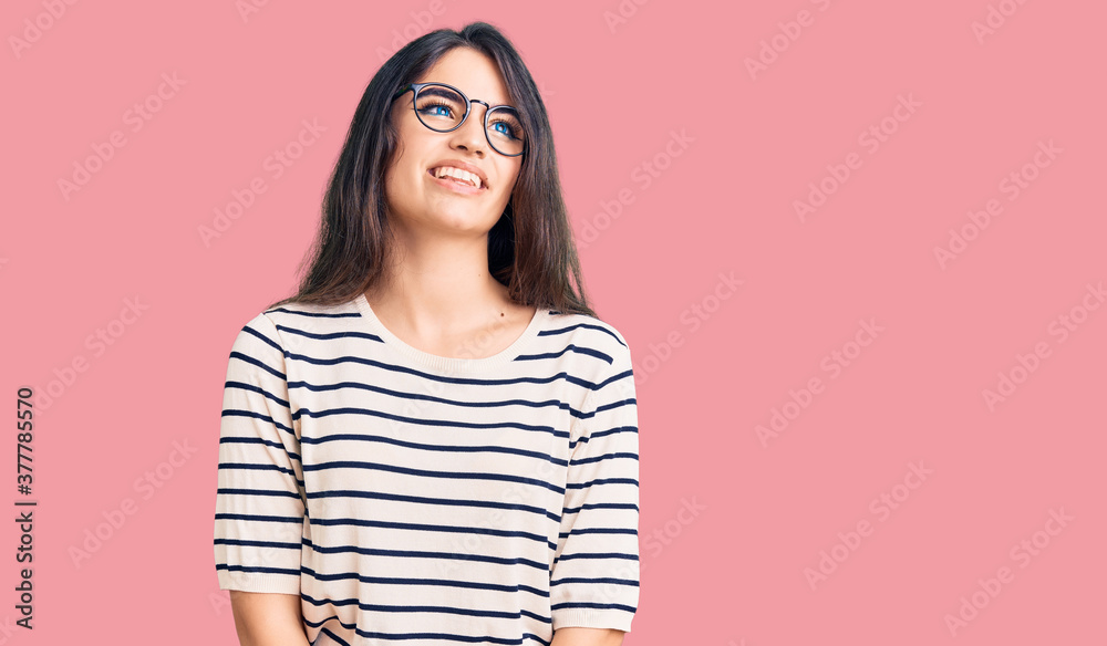 Brunette teenager girl wearing casual clothes and glasses looking away to side with smile on face, natural expression. laughing confident. Brunette teenager girl wearing casual clothes and glasses looking away to side with smile on face, natural expression. laughing confident.