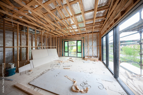 Interior view of a modern house undergoing construction, with timber frames, sliding glass doors and trusses