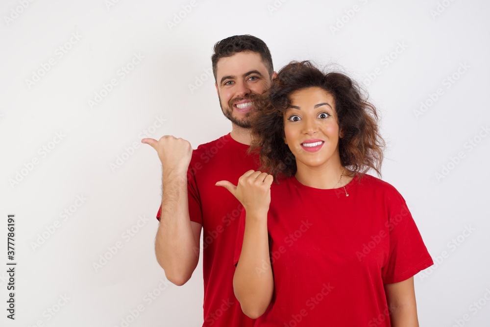 Lovely Young beautiful couple wearing red t-shirt on white background pointing aside with forefinger, showing at copy space having news about bargains Lovely Young beautiful couple wearing red t-shirt on white background pointing aside with forefinger, showing at copy space having news about bargains