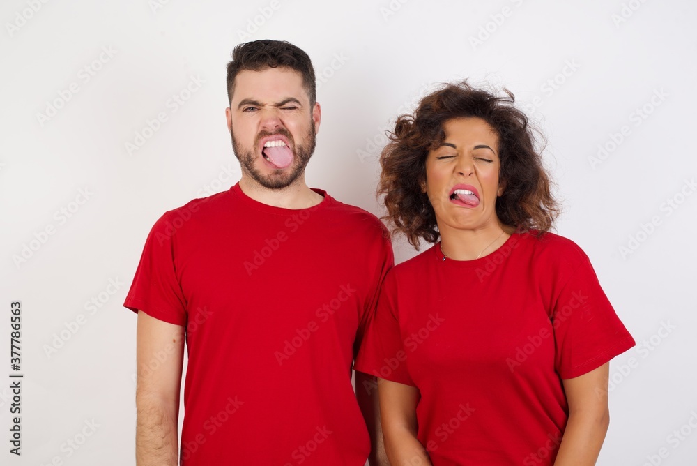 Fototapeta premium Young beautiful couple wearing red t-shirt on white background sticking tongue out happy with funny expression. Emotion concept.