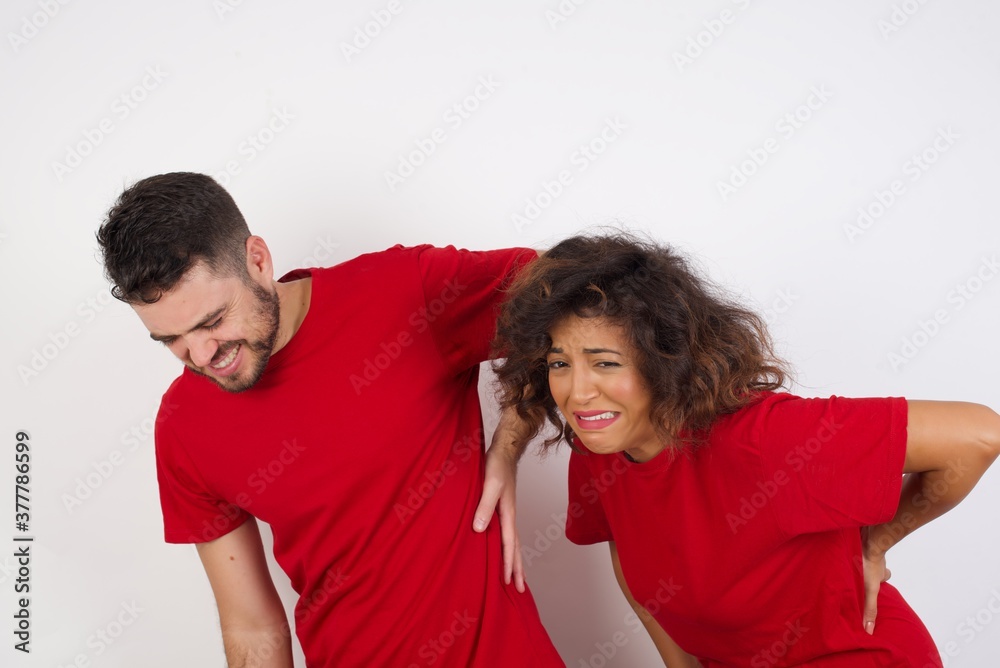 Obraz premium Young beautiful couple wearing red t-shirt on white background Suffering of backache, touching back with hand, muscular pain
