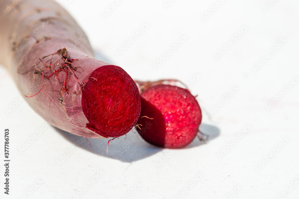 A single long deep red cylinder shape beet recently cut with a sharp knife. It's a long red stalk.  The bright red vegetable sits on a white background. There's a pattern in the center of the beet.