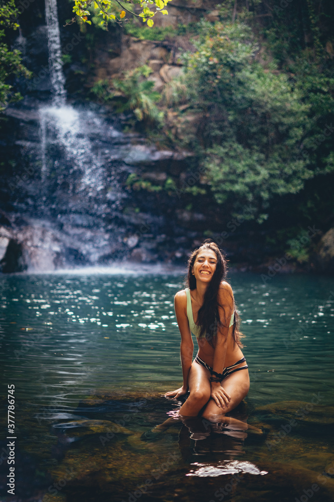 Chica en bikini en un lago con cascada tropical en una gruta verde de los arcornocales de vacaciones