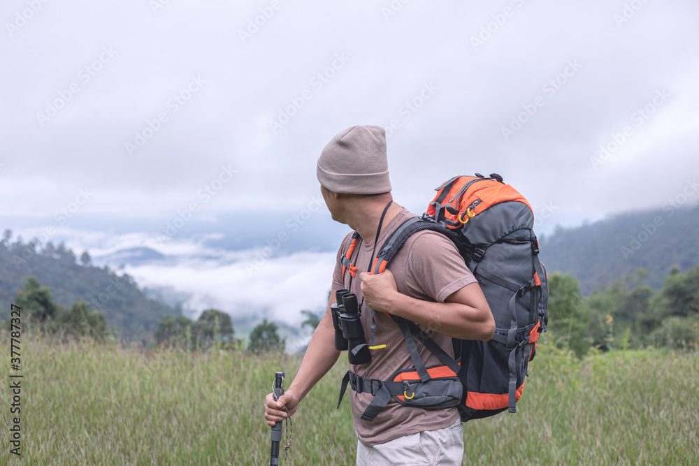 Young man with backpack and binoculars looks foggy mountain landscape Young man with backpack and binoculars looks foggy mountain landscape