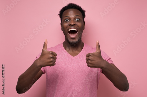 Handsome black man showing thumb up with cheerful attitude on pink background