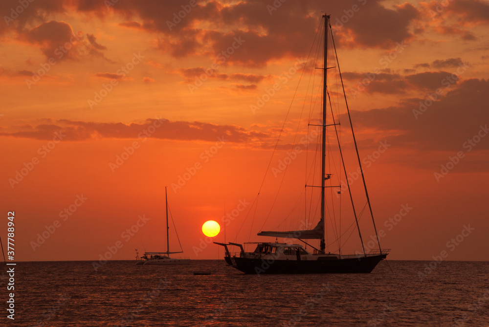 Sailboat stop on the sea at sunset and two sailboat against a vivid colorful sunset.
