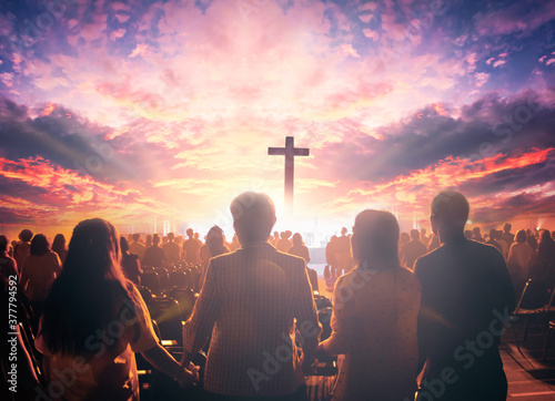 Worship concept: christian people hand in hand over cross on spiritual sky background
