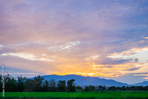 beautiful warm colorful sunrise or stunning sunset at a large mountain  with green rice field scenery in summer farming time  Asian county  or agriculture countryside. landscape background texture.