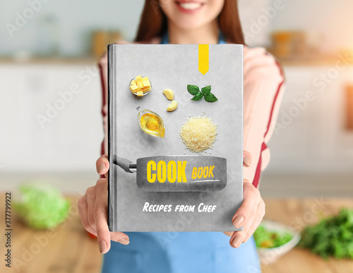 Young woman with cook book in kitchen, closeup photo