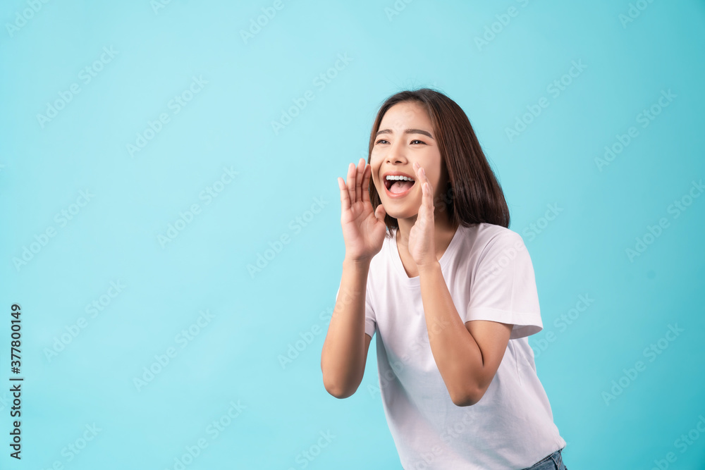 Young Asian woman standing on a blue background and hand touches on mouth with yelled for something. Young Asian woman standing on a blue background and hand touches on mouth with yelled for something.