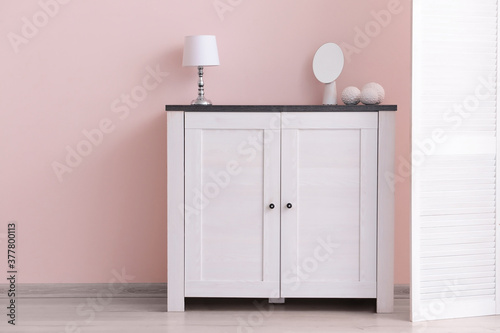 Modern chest of drawers with lamp and mirror near color wall in room