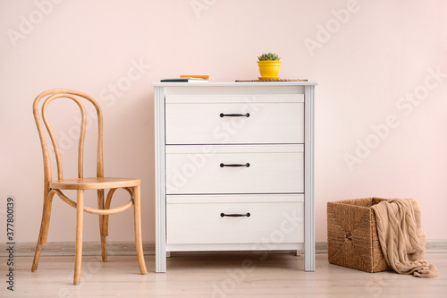 Modern chest of drawers with chair near color wall in room © Pixel-Shot