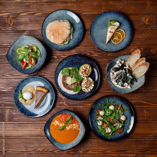 Different meals of european cuisine, placed in a circle, on a dark wooden table, top view