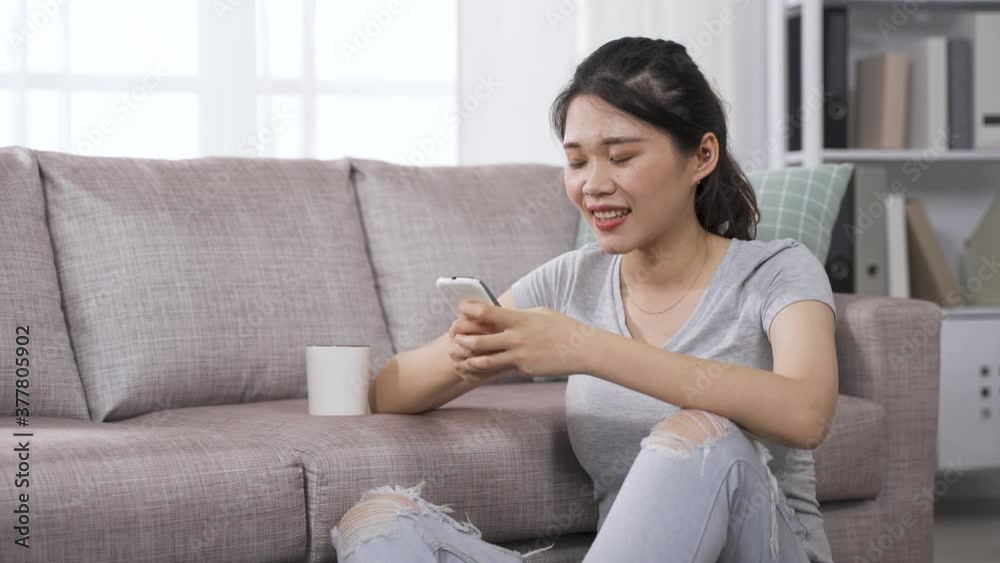 asian girl drinking tea and playing games on phone in her leisure time in the cozy living room at home asian girl drinking tea and playing games on phone in her leisure time in the cozy living room at home