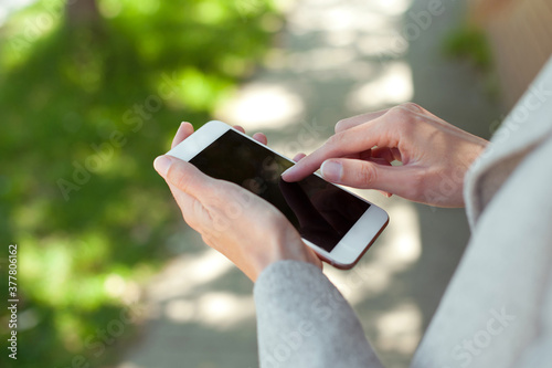 Young woman holding a white smartphone in hands. Outdoor. 