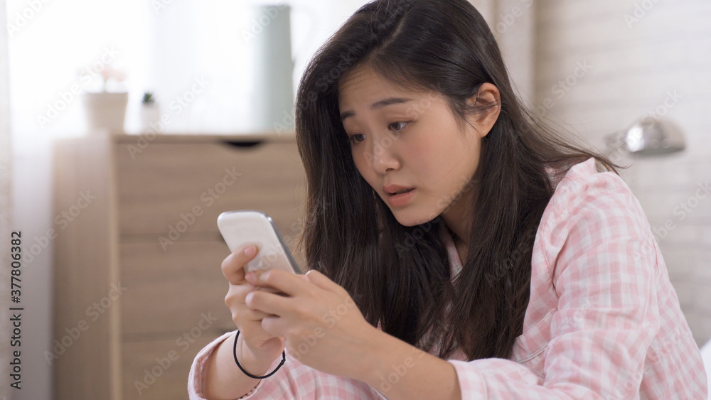 closeup asian lady looking at smartphone screen is confused by the notification and trying to figure it out in bright bedroom. closeup asian lady looking at smartphone screen is confused by the notification and trying to figure it out in bright bedroom.