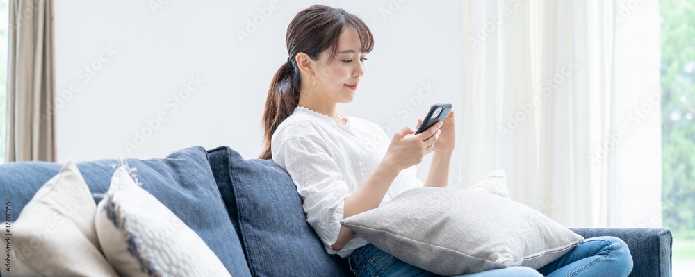 Fototapeta premium 家で携帯を触るアジア人女性 
