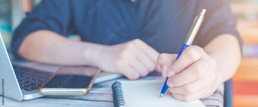 Woman is writing on a notebook with a pen and she is using a mobile phone in the office.