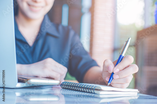 Obraz na płótnie Woman is writing on a notebook with a pen and she is using a mobile phone in the office. w salonie