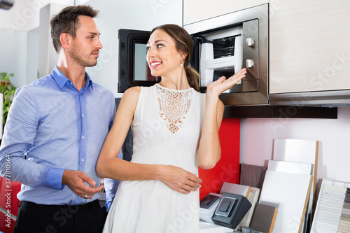 Young happy cheerful positive couple choosing microwave in household appliance section in furnishing store