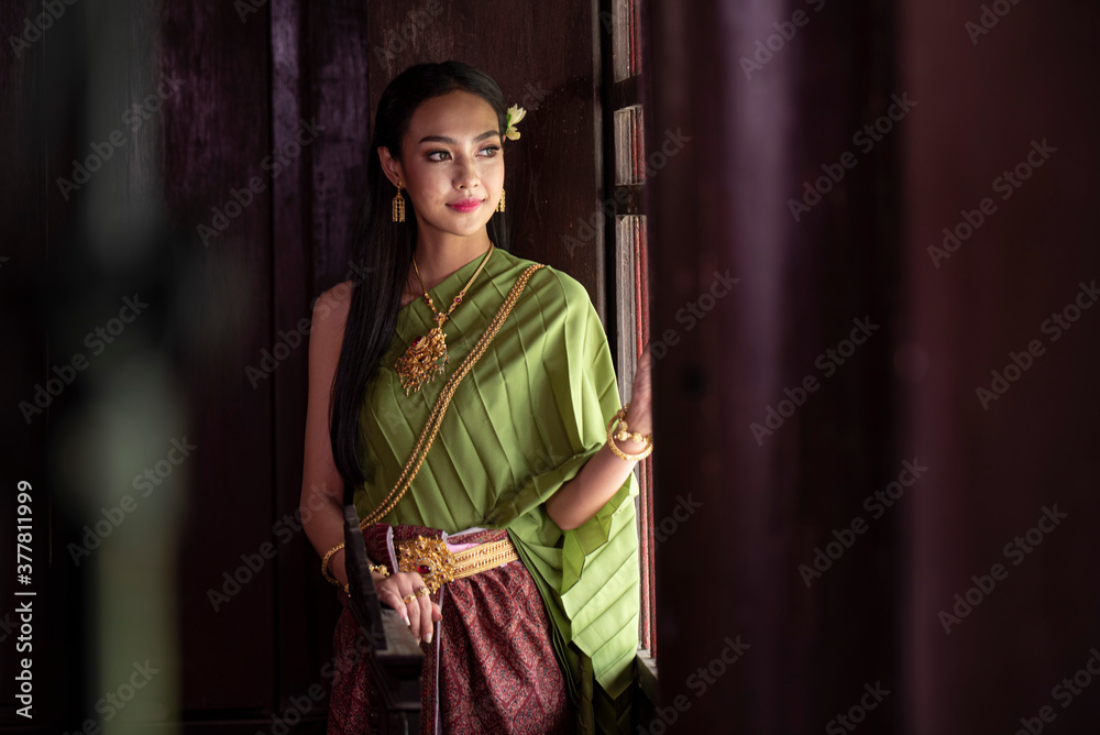 Portrait of a beautiful woman in Thai old suit or Thai national dress suit looks elegant and charming in Old antique Thai houses/Old Thai fashion model concept Portrait of a beautiful woman in Thai old suit or Thai national dress suit looks elegant and charming in Old antique Thai houses/Old Thai fashion model concept