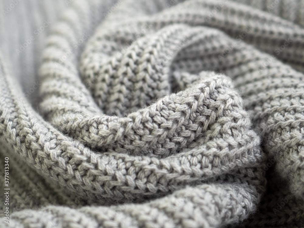 Knitted warm grey sweater or scarf. Cozy composition in the home atrosphere. Wool fabric texture close up background. Comfortable style cloth. Wavy folds material. Soft focus Knitted warm grey sweater or scarf. Cozy composition in the home atrosphere. Wool fabric texture close up background. Comfortable style cloth. Wavy folds material. Soft focus