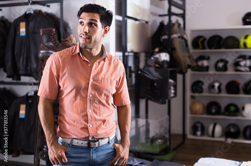 Adult positive european man is posing near modern equipment for motorbike in the store.