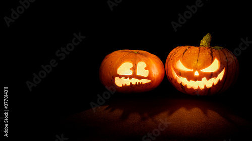 Two Halloween pumpkins with glowing eyes and mouth on a black background with copy space. One pumpkin with a scary face, another with a scared face