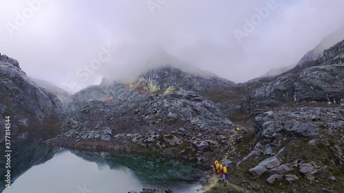 A group of people hiking on the side of huge epic lake on wonderful Mount Carstensz, Sudirman mountain range, Papua, Indonesia camera tilt down photo