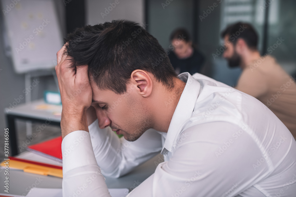 Tired dark-haired male sitting at meeting, resting his head on his hands Tired dark-haired male sitting at meeting, resting his head on his hands