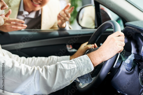Close-up of man sitting and holding the wheel while testing a new car together with salesman in car showroom