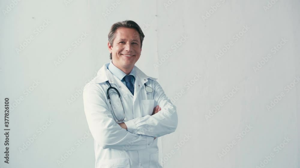 doctor in white coat with stethoscope standing with crossed arms on grey doctor in white coat with stethoscope standing with crossed arms on grey