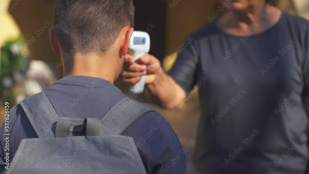 Teacher checking the temperature to a schoolboy before cpming into the school. Covid-19 Coronavirus prevention. Education, lifestyle. 