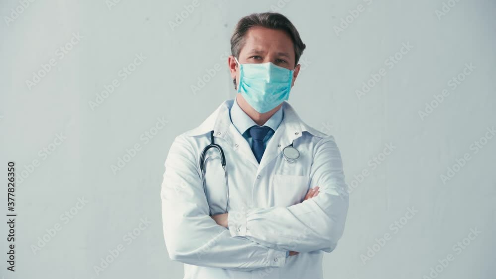 doctor in white coat and medical mask standing with crossed arms on grey doctor in white coat and medical mask standing with crossed arms on grey