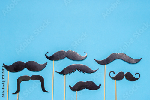 Various black photo booth props moustaches of different shape on blue background. Greeting card for father's day or men's health awareness month campaign concept. Flat lay, space for text, mock up