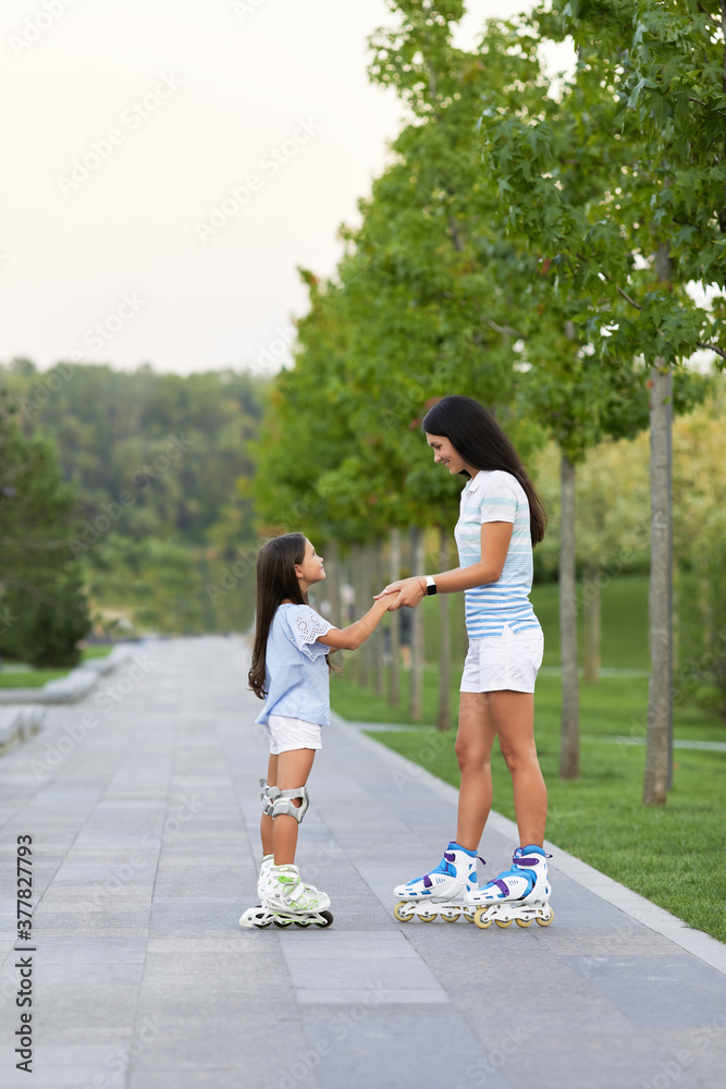 Young mother and her pretty little daughter rollerskating in summer park. happy family have fun Young mother and her pretty little daughter rollerskating in summer park. happy family have fun