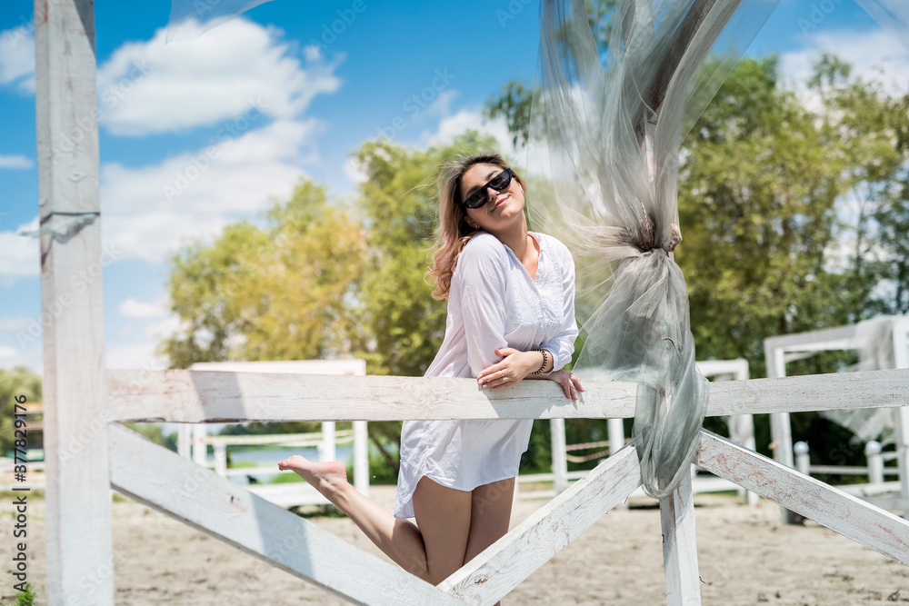 Pretty girl enjoy nature at sunny day in white wooden gazebo near the lake
