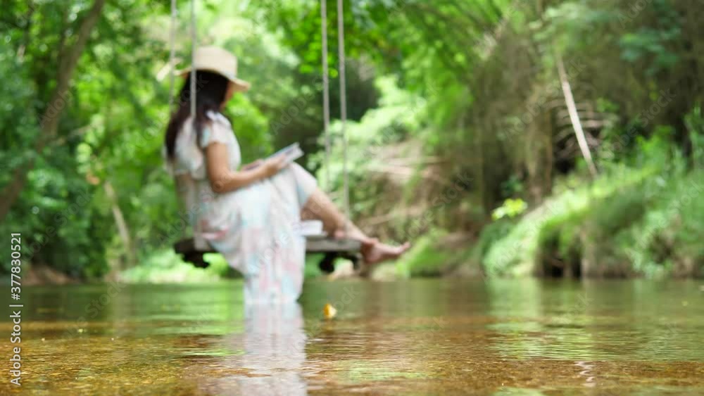 Water stream. A river flows in beautiful scene and woman sitting on wood swing hanged on a tree and reading book.
Water stream. A river flows in beautiful scene and woman sitting on wood swing hanged on a tree and reading book.