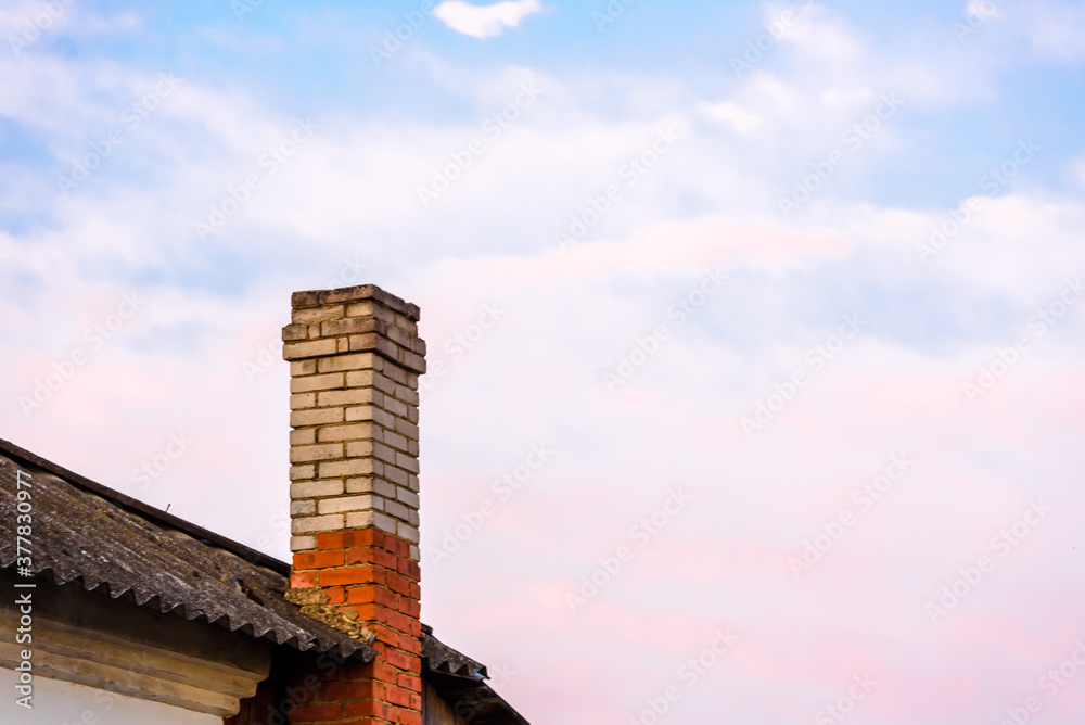 Chimney on the roof of a house against a beautiful blue sky with pink clouds. The time of sunset.