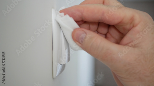 Image with Man Hand Disinfecting a Lights Switch Using a Wet Wipe and Disinfectant Solution