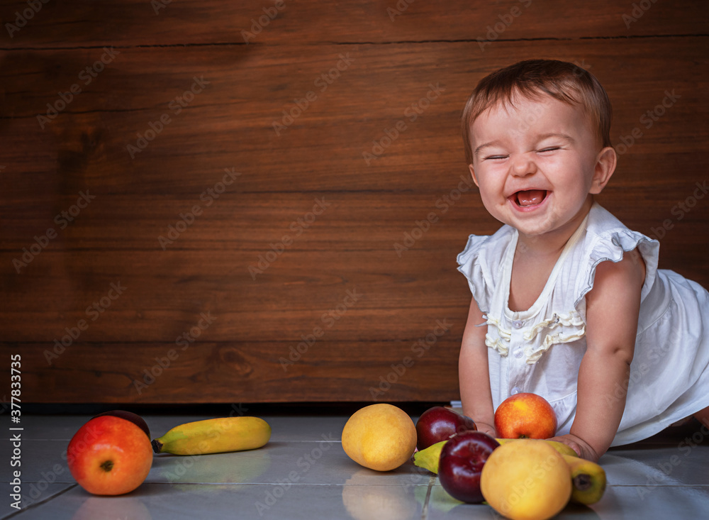 Fototapeta premium happy cute baby crawling on the floor with fruits apples, plums, bananas, mango on the wooden background