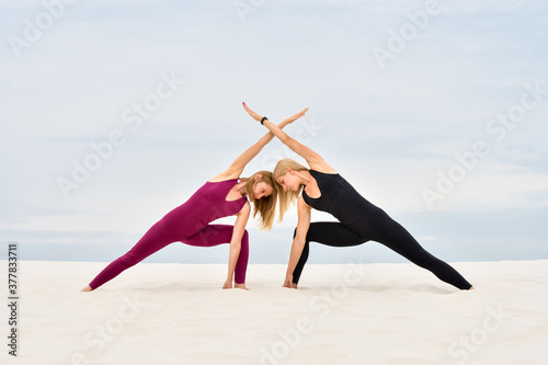 Two beautiful young women performing together yoga pose parshvakonasana photo
