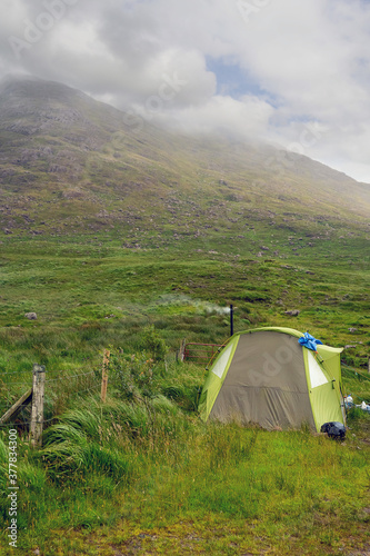 Small tent set up in a field  Smoke coming out from chimney  Mountain in fog in the background  Low clouds  Connemara  Ireland  Travel and outdoor adventure concept.