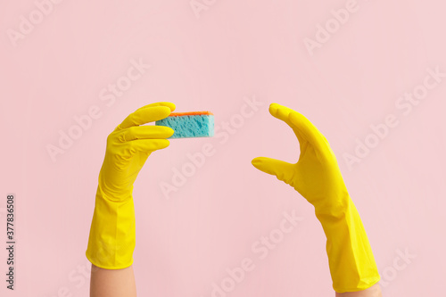 Hands in rubber gloves and with sponge on color background