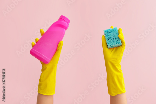 Hands in rubber gloves holding sponge and detergent on color background