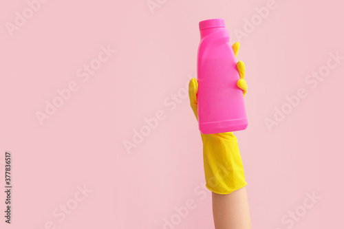 Hand in rubber glove holding detergent on color background