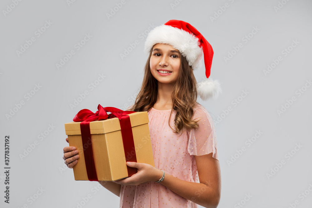 christmas, holidays and people concept - happy smiling teenage girl in santa helper hat holding gift box over grey background christmas, holidays and people concept - happy smiling teenage girl in santa helper hat holding gift box over grey background