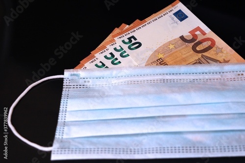 A medical mask lies on euro banknotes. Economy and coronavirus concept.