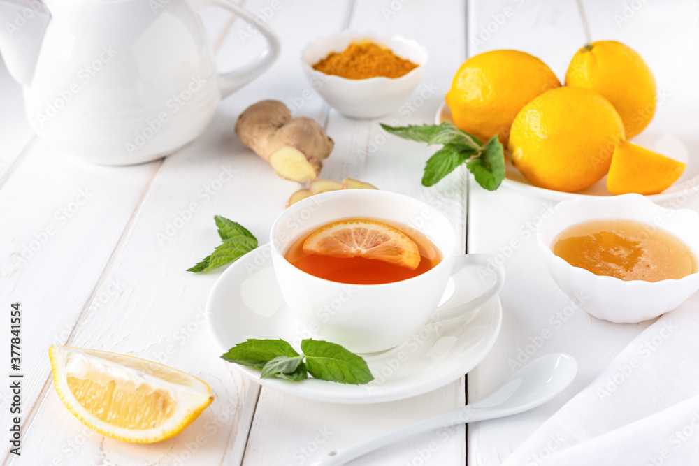 Antioxidant healthy tea with lemon, ginger, honey, turmeric and mint on a white wooden table. The concept of alternative medicine. Antioxidant healthy tea with lemon, ginger, honey, turmeric and mint on a white wooden table. The concept of alternative medicine.